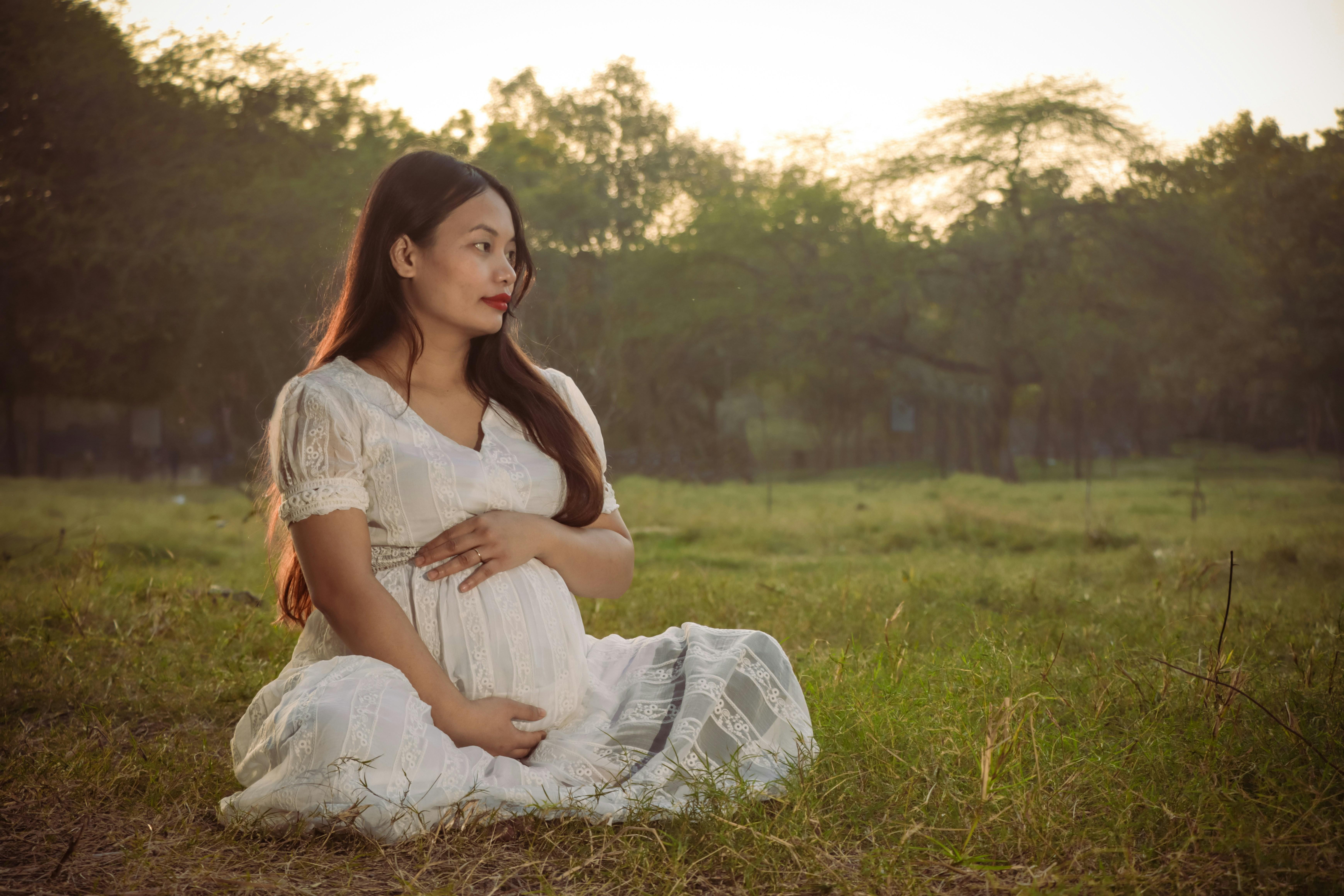A pregnant woman in a white dress sits in a field