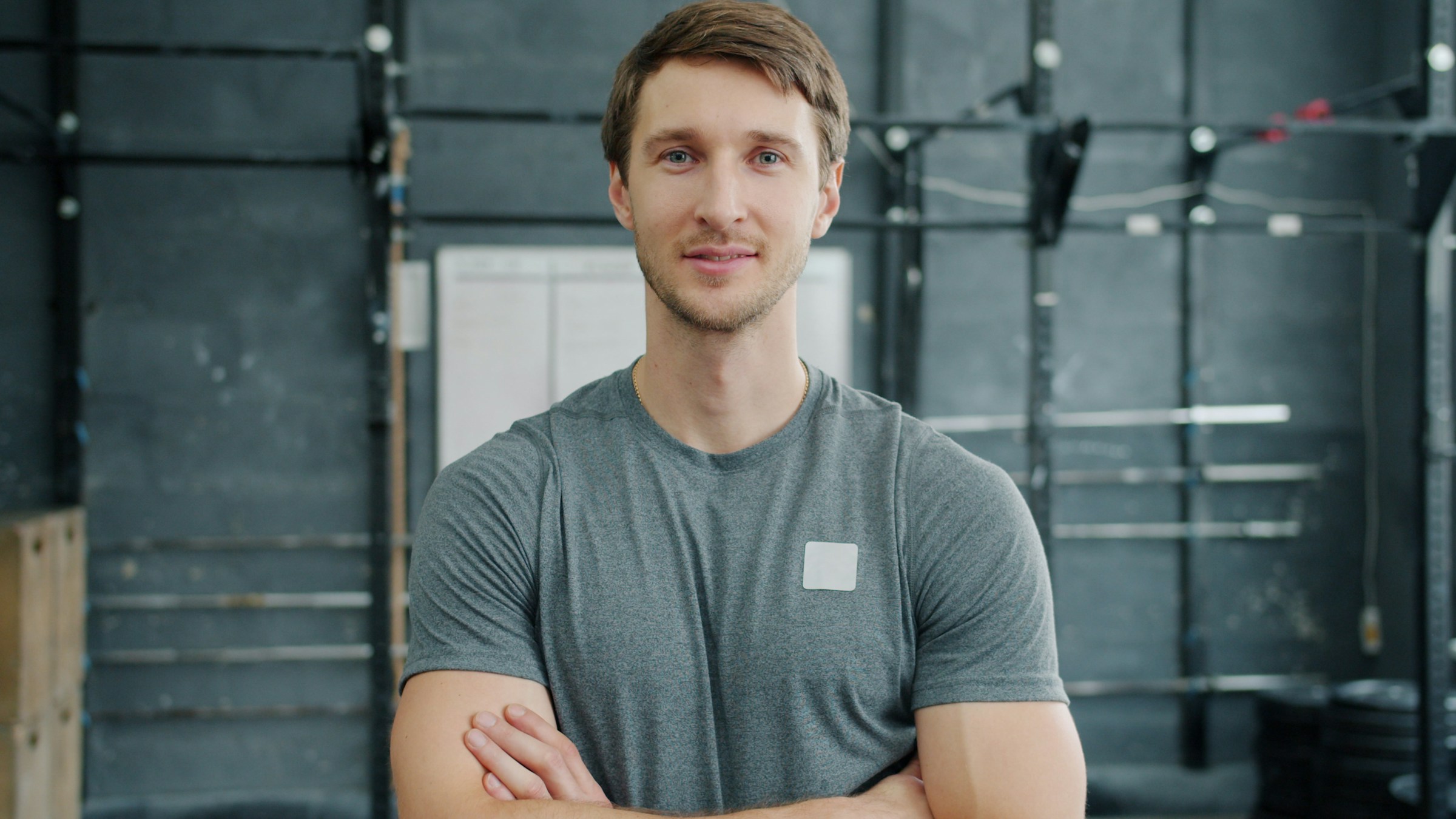 An athletic man stands in a gym with his arms crossed