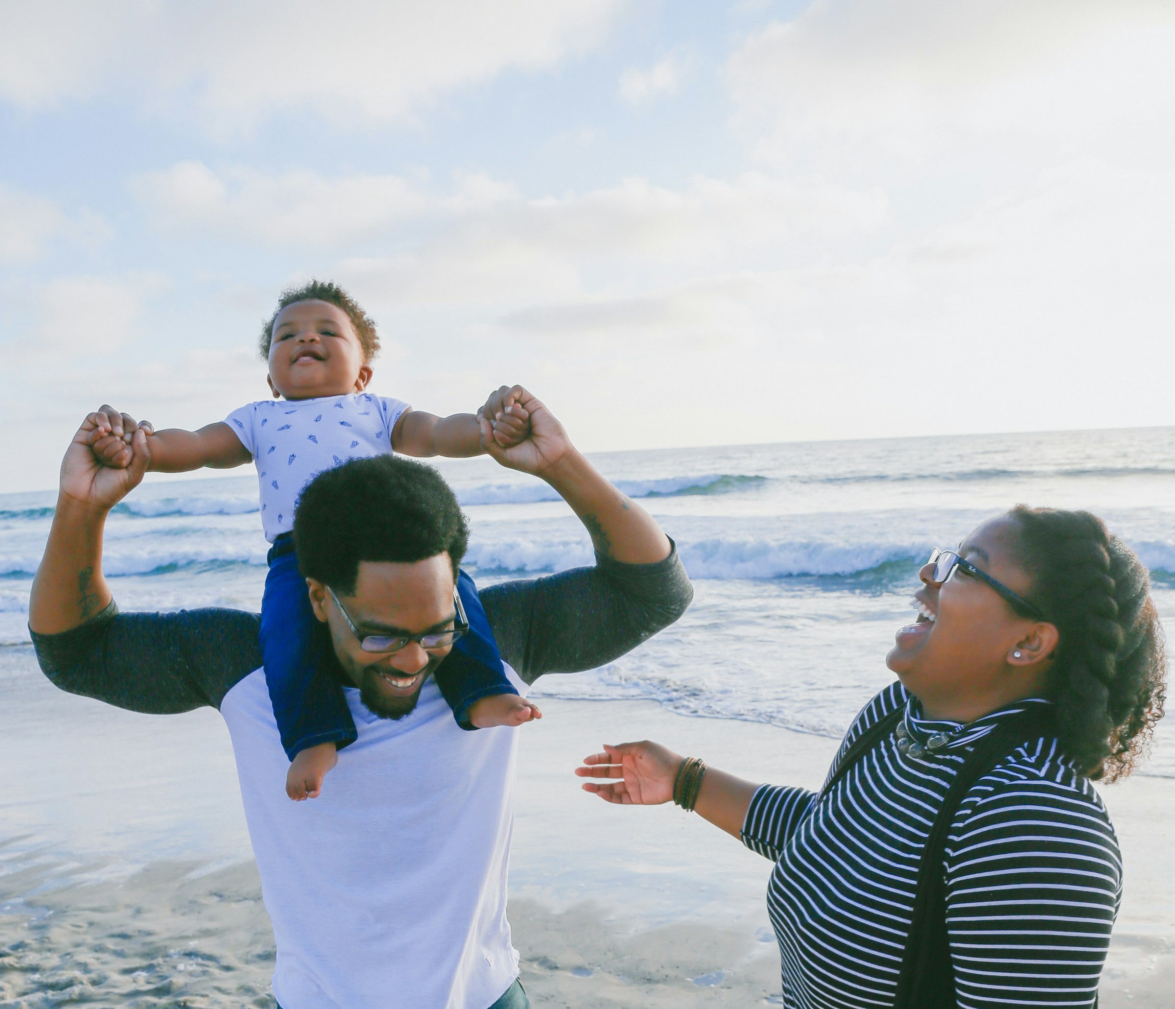 A couple walks with their baby along a beach