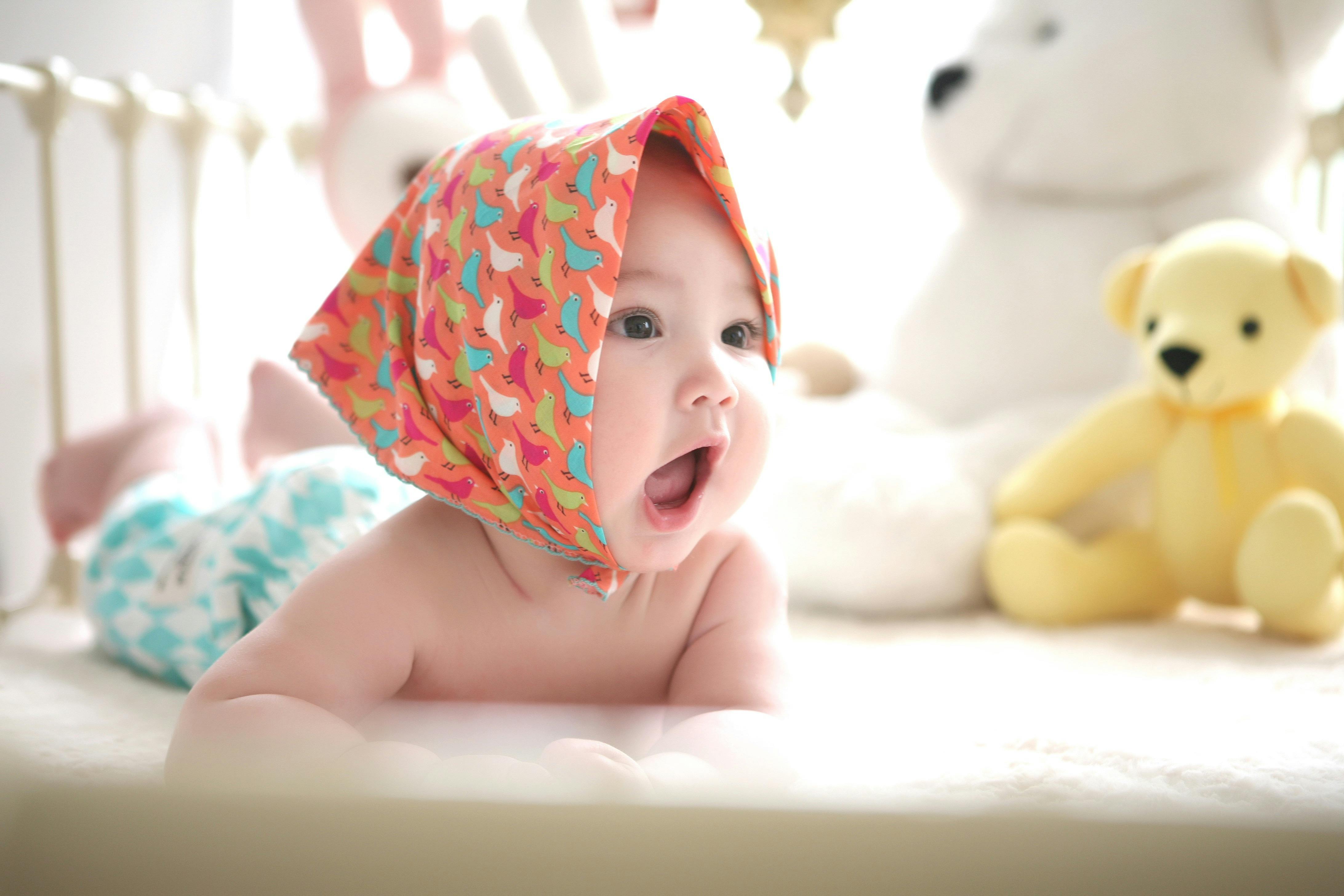 Baby with wide-open mouth lying in a cot with teddies
